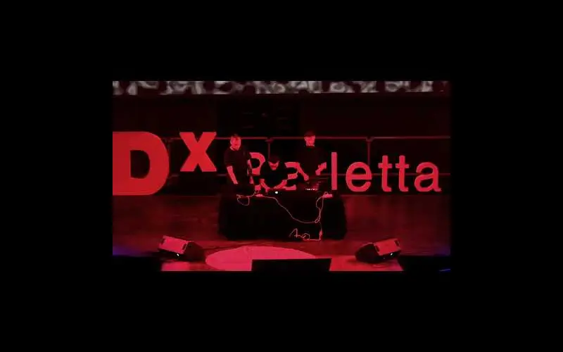 Performers silhouetted against a red TEDx Barletta stage